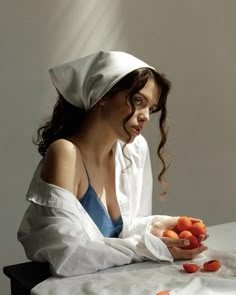 a woman sitting at a table with carrots in her hands and wearing a chef's hat