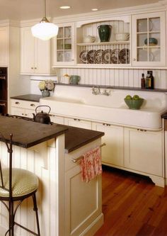 a kitchen with white cabinets and black counter tops, an island in the middle is flanked by two stools