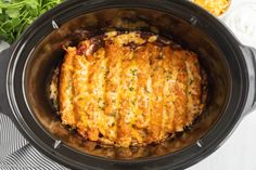 a crock pot filled with meat and cheese sitting on top of a table next to vegetables