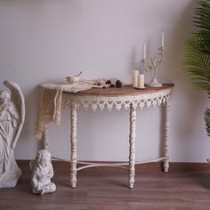 a white table with angel figurines and candles on it next to a potted plant