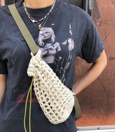 a woman is holding a crocheted bag in her right hand and wearing a necklace