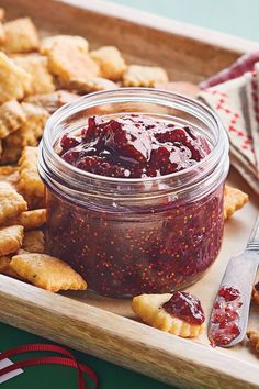 a wooden tray topped with cookies and jelly next to a jar of strawberry jam on top of crackers