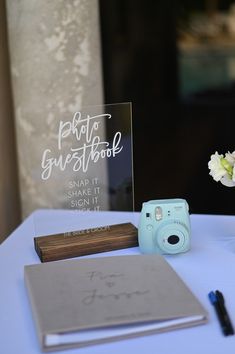 a table with a camera, notebooks and flowers on it next to a sign that says photo guestbook