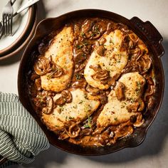 a skillet filled with chicken and mushrooms on top of a white table next to silverware