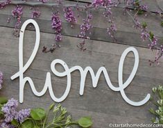 the word home is made out of white wood and surrounded by purple flowers on a wooden wall