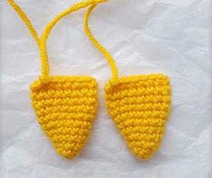 two crocheted yellow triangle shaped objects hanging from strings on a white surface,