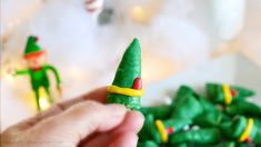 a hand holding a small green toy elf