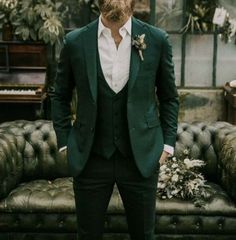 a man with a beard wearing a green suit and white shirt standing in front of a couch