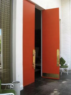 two orange doors are open on the outside of a building with chairs and tables in front of them