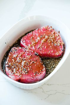 two pieces of meat in a white bowl with seasoning on top and black pepper sprinkles