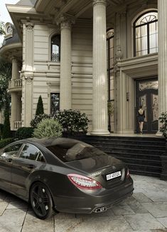 a black car is parked in front of a large house with columns and pillars on the side