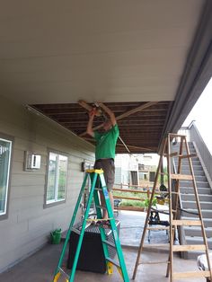 a man standing on top of a step ladder next to a green scaffolding