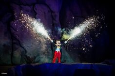 mickey mouse on stage with fireworks coming out of his ears and hands in the air