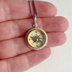 a person holding a compass necklace in their hand