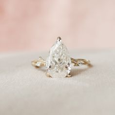 a pear shaped diamond sits on top of a gold band and is surrounded by leaves