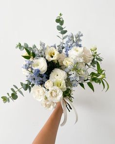 a bouquet of white and blue flowers in someone's hand on a white background