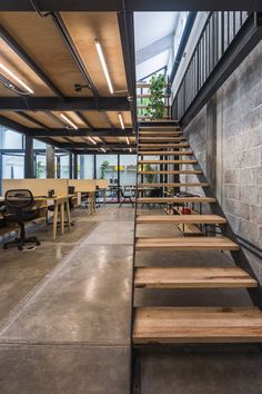 an office with concrete walls and wooden stairs leading up to the second floor, along with tables and chairs