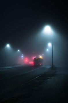 the bus is driving down the street in the foggy night with its lights on