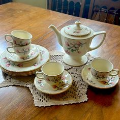 a wooden table topped with china cups and saucers on top of a doily