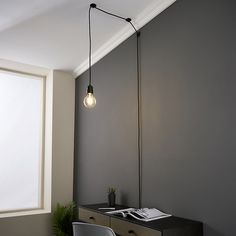 a lamp hanging over a desk next to a window with a potted plant on it