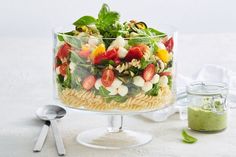 a glass dish filled with pasta salad next to a jar of green pesto dressing