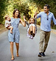 a man and woman walking down the street with two small children in their arms while holding hands