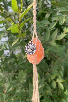 an orange piece of glass hanging from a rope on top of a leafy tree