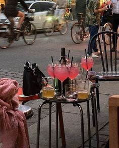 two tables with drinks sitting on top of it next to a street filled with people