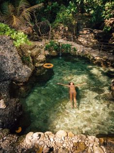 a person in the water with a frisbee and trees behind them, surrounded by rocks