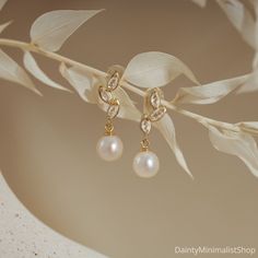 a pair of gold earrings with pearls hanging from it's earwires on a leafy branch