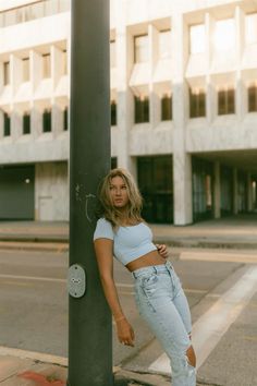 a woman leaning against a pole on the street