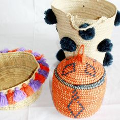 two woven baskets with pom - poms on them, one in orange and the other in purple