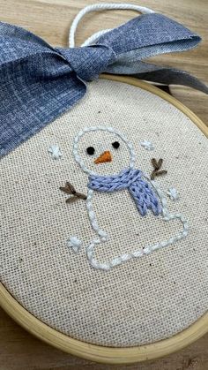 a snowman with a blue scarf on it's head is sitting in front of a wooden hoop