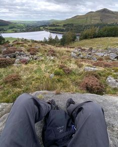 someone is sitting on top of a rock with their feet in the air, overlooking a lake and mountains