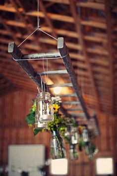 several mason jars hanging from the ceiling in a barn with sunflowers and greenery