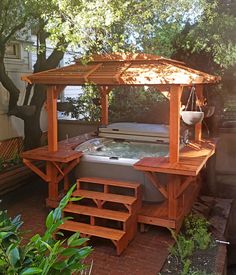 a hot tub sitting under a wooden gazebo next to a lush green tree and shrubbery