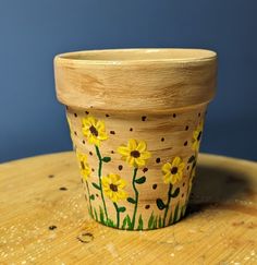 a flower pot sitting on top of a wooden table with yellow flowers painted on it