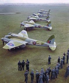 a group of men standing next to each other in front of fighter jets on top of a grass covered field