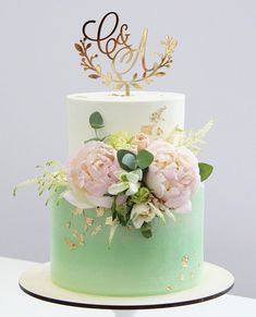 a green and white cake with flowers on the top is decorated with gold leaf accents