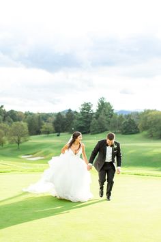 a bride and groom walking across a green golf course in front of the camera on their wedding day