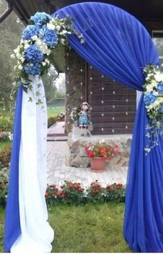 an outdoor ceremony with blue drapes and white flowers on the side of the arch