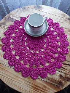 a cup and saucer on a wooden table with a pink crochet doily