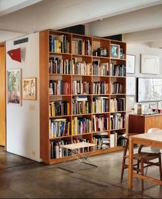 an open bookcase with many books on it in a living room next to a dining room table