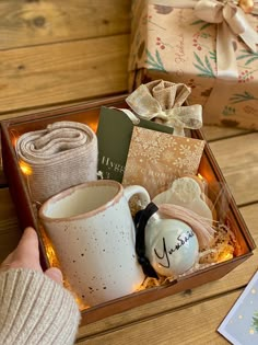 a person is holding a box with christmas items in it and wrapped presents on the table