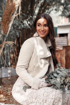 a woman is sitting on a bench with flowers in her hand and smiling at the camera