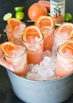 a person holding up some orange slices in a metal bucket with ice and limes around it