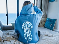 Stay cozy with this hibiscus jellyfish hoodie on those cool days and nights. Any beachy jellyfish lover would be happy with this hoodie! 🤩 TIP: These sweaters run true to size. If you want an oversized look, size up 2-3 sizes. 😉 ➡️ Design is printed on back of hoodie. The front is blank ⬅️ ✅ Information: ★ Gildan Unisex Hoodie ★ -50% Cotton 50% Polyester -Medium-heavy fabric -Classic fit -Tear away label -Runs true to size ✅Design Printing Design printed using Direct to Garment (DTG) print technology. ✅ Care Instructions Due to the ink used in the design, please wash it inside out in cold water. Allow the item to air dry for lasting print quality. ✅ Processing time and Shipping It typically takes 4-7 business days to process orders in the US. However, around holidays or weekends, this ti Blue Summer Hoodie With Drawstring Hood, Blue Hooded Hoodie For Vacation, Beachy Hoodies, Jellyfish Hoodie, Ocean Clothes, Beach Hoodies, Ocean Outfits, Sea Life Animals, Save The Ocean