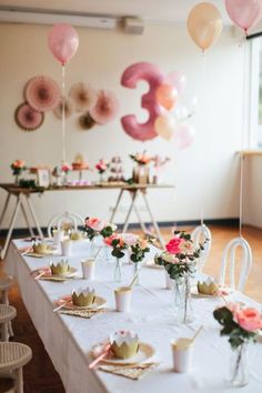 a long table topped with lots of plates and cups filled with food next to balloons