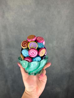 a hand holding a glass bowl filled with colorful candies on top of each other