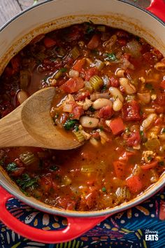 a red pot filled with beans and other food on top of a colorful table cloth